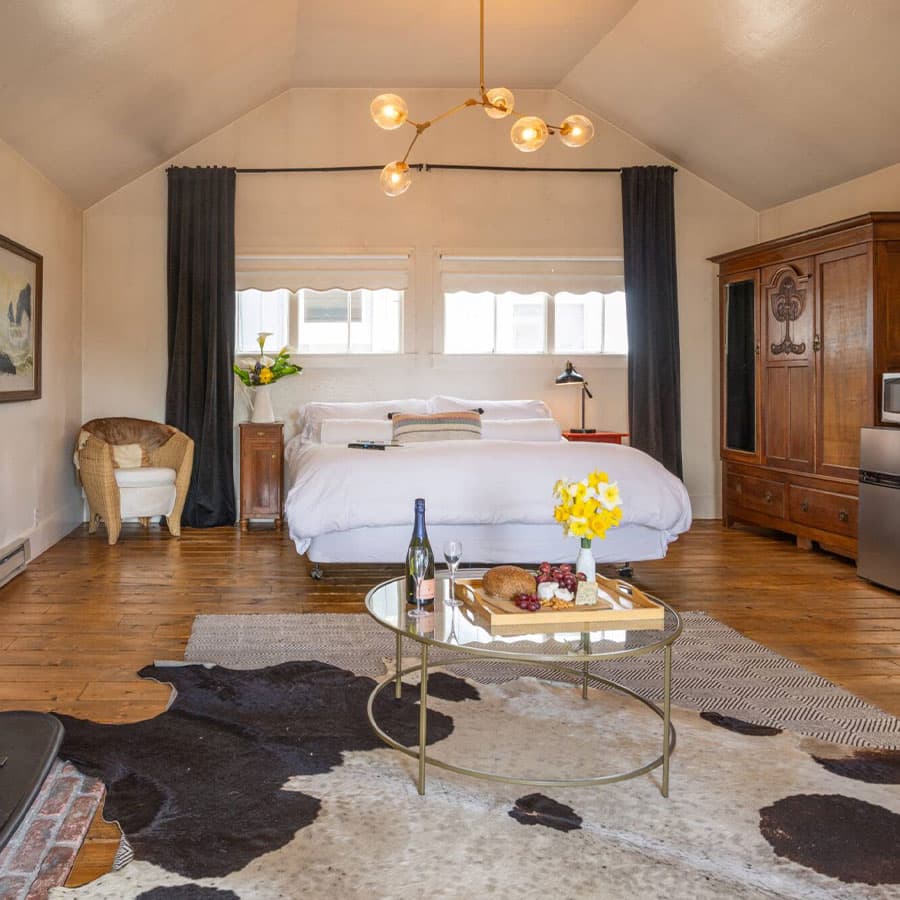 A luxurious bedroom with a plush king-size bed, a cozy fireplace, and a glass coffee table set with wine and snacks.