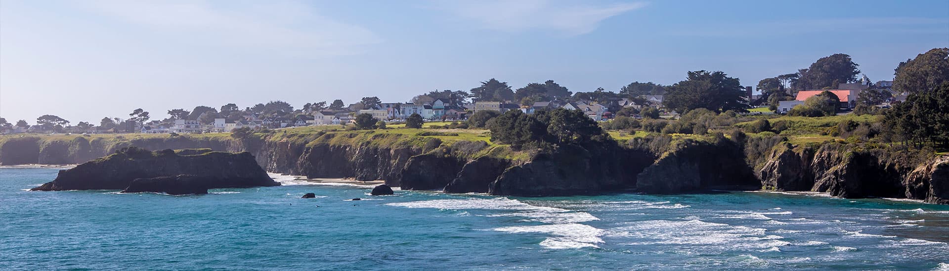 A panoramic view of the Mendocino Coast, with rugged cliffs, crashing waves, and a small town nestled on the hillside.