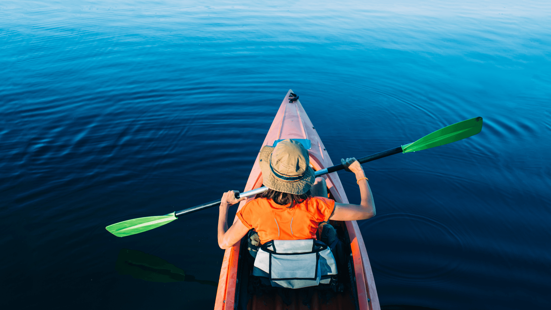 A person paddles a kayak on calm blue water.