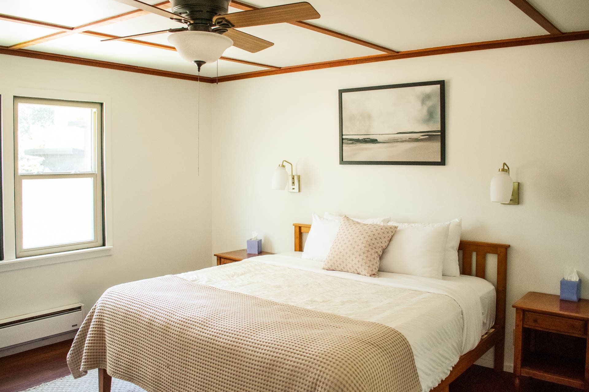 Cozy, well-lit bedroom featuring a double bed, artwork, and wooden furniture.