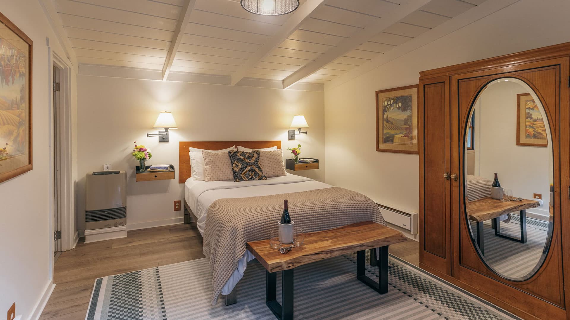 Cozy bedroom with a queen-size bed, wooden armoire, and wine bottle on a bench.