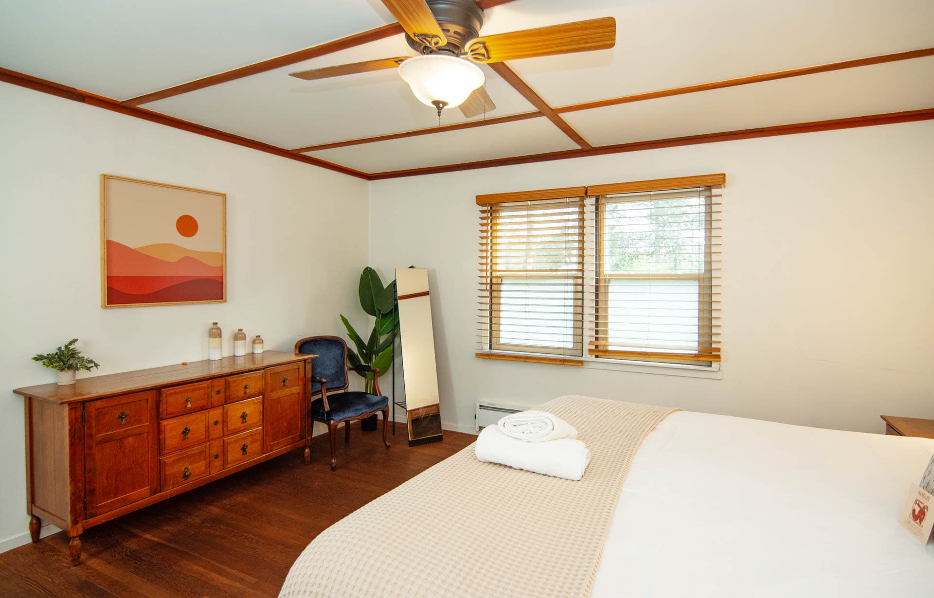 Cozy bedroom featuring a bed, dresser, chair, and large windows with natural light.
