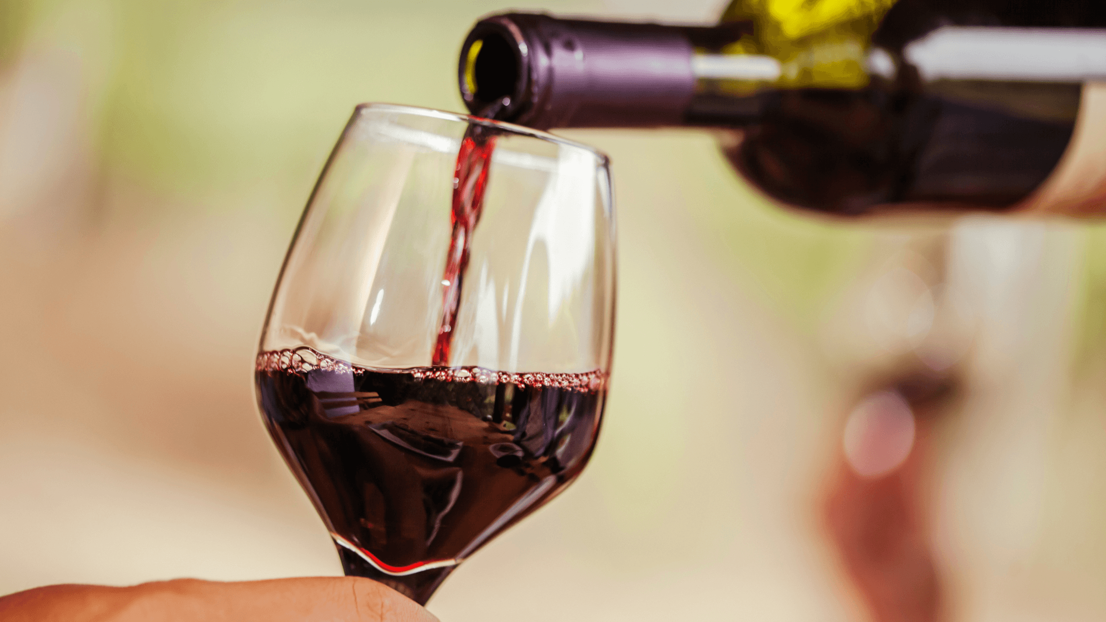 A glass being filled with red wine from a bottle. A glass being filled with red wine from a bottle.