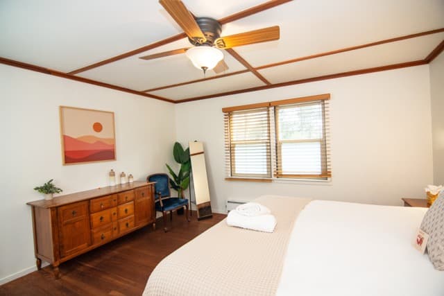 Bright and spacious bedroom with cozy bedding, warm wood accents, and modern decor for a relaxing retreat stay.