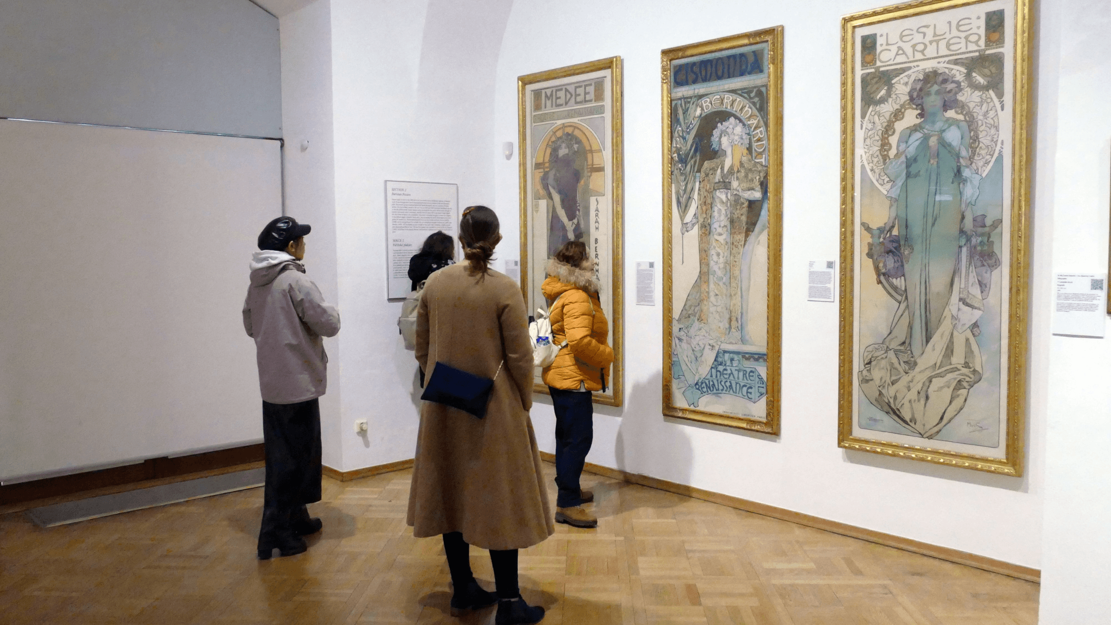 Four visitors admire art nouveau posters in a museum.