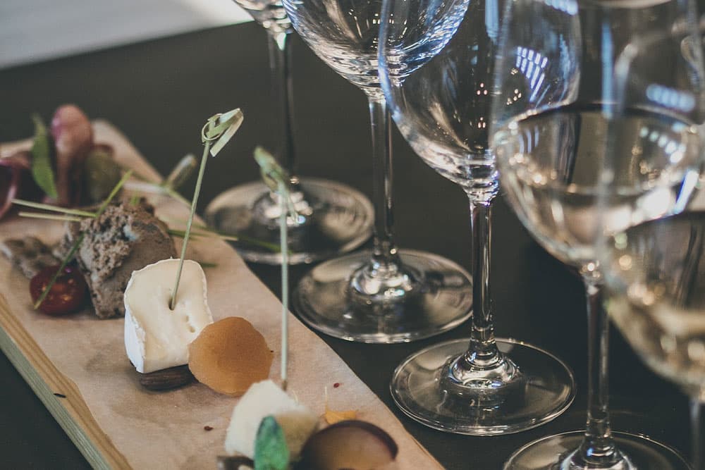 A selection of artisanal cheeses, charcuterie, and fruit, paired with a flight of wine, presented on a wooden board.