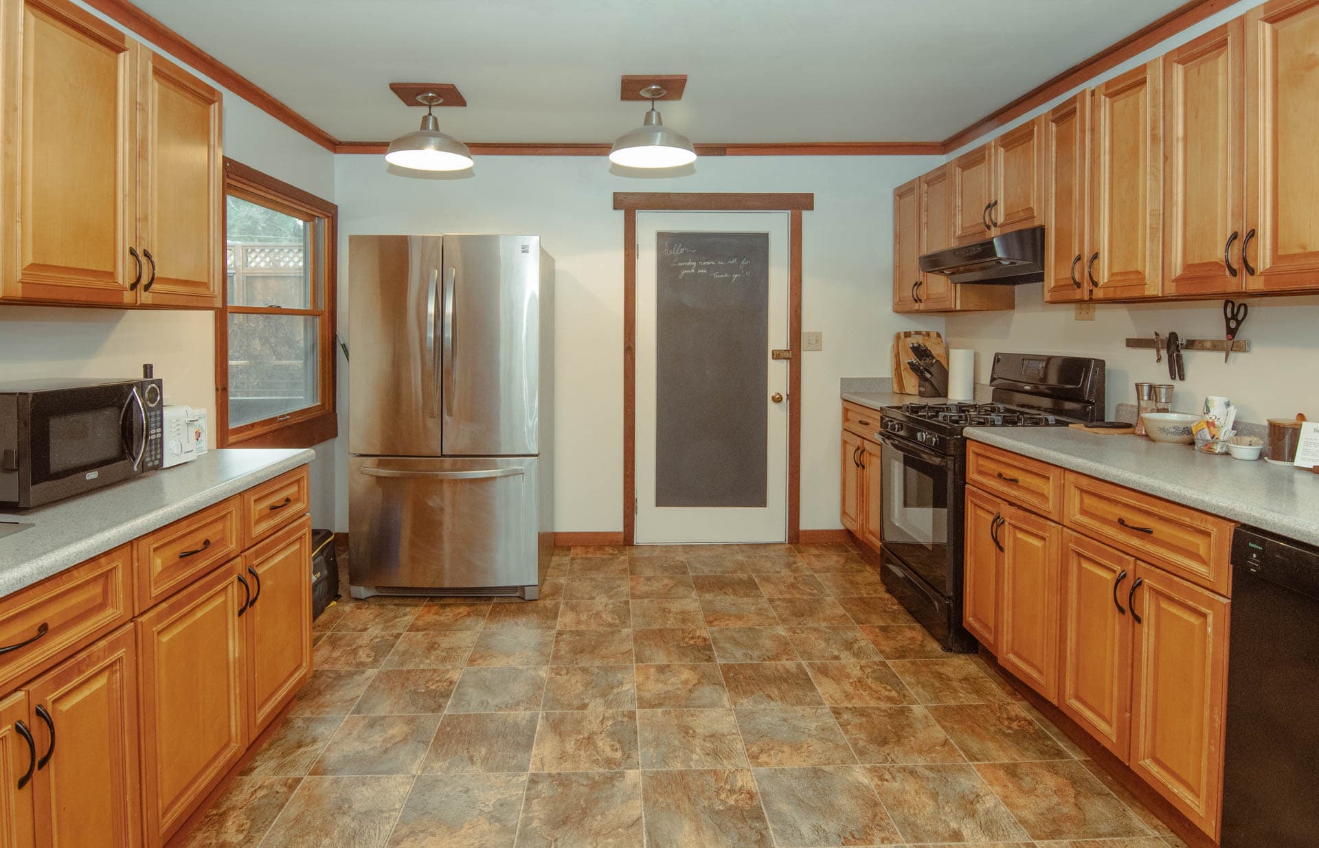 A modern kitchen with wooden cabinets, stainless steel appliances, and a tiled floor.